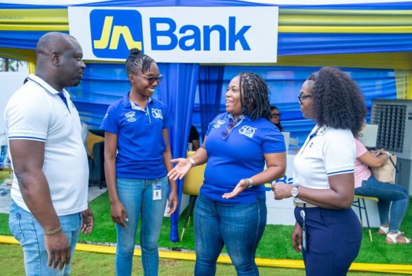 Four people chat at an outdoor Jn Bank booth under a blue-yellow canopy, smiling and engaging.